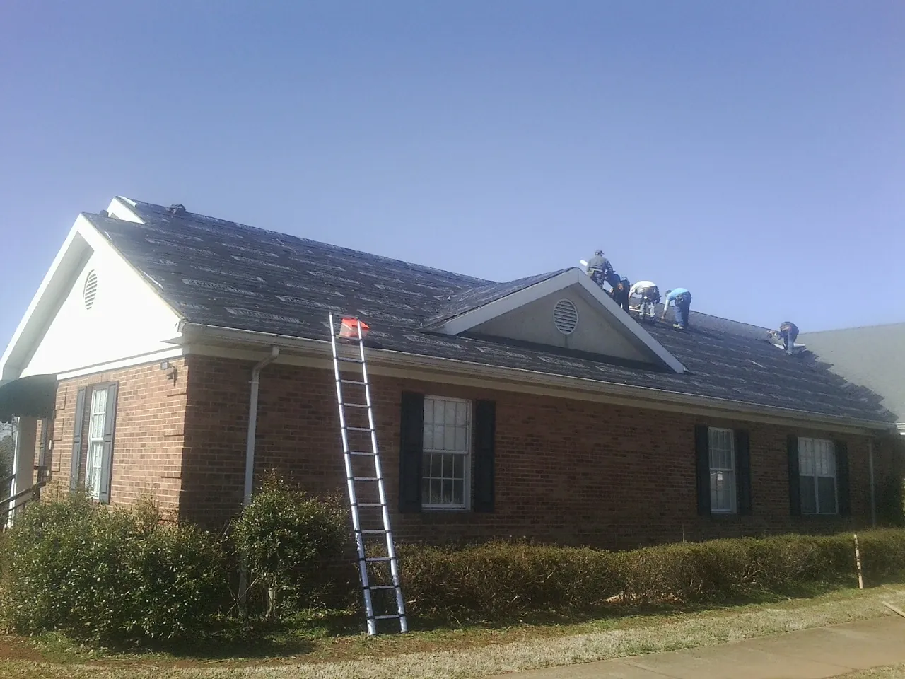 Crew tearing shingles off a brick ranch roof with a ladder set — Metal Roof Repair work by our crew in Edgewood