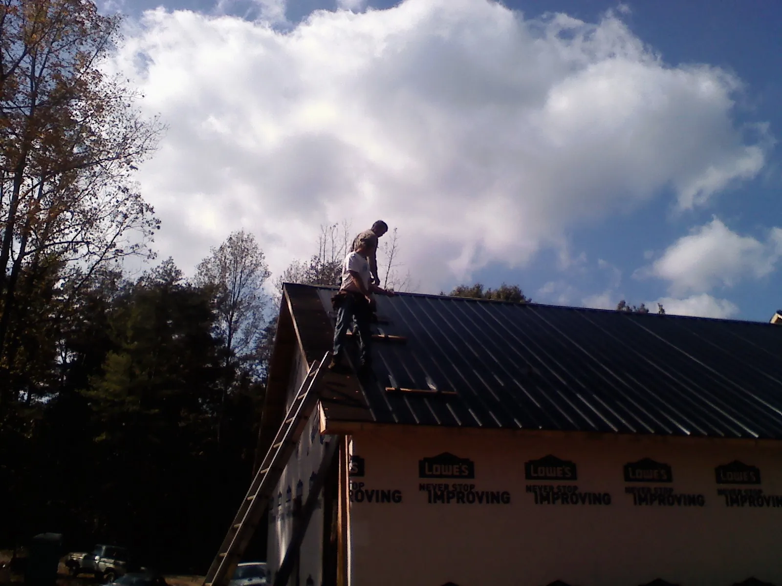 Roofer fastening dark metal panels high against a cloudy sky, from a Roof Inspection job in Edgewood