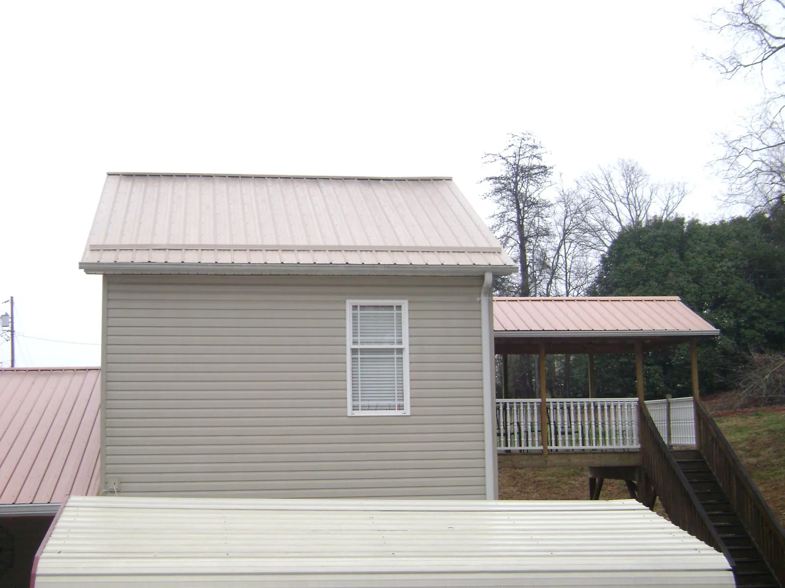 Tan metal roofs on a two story addition and attached porch, from a Roof Replacement job in Edgewood